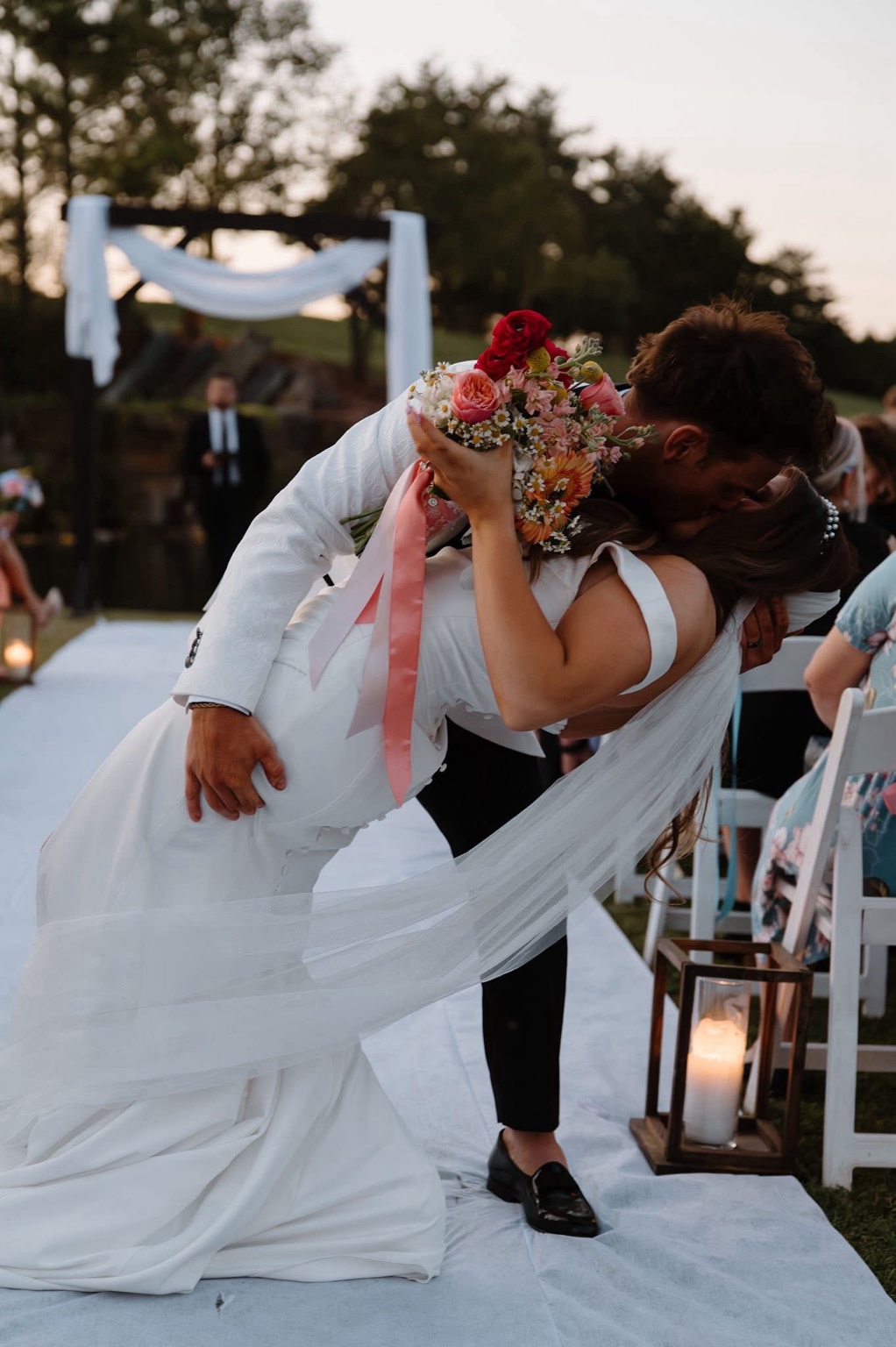 A newly married couple sharing a celebratory kiss on an outdoor aisle