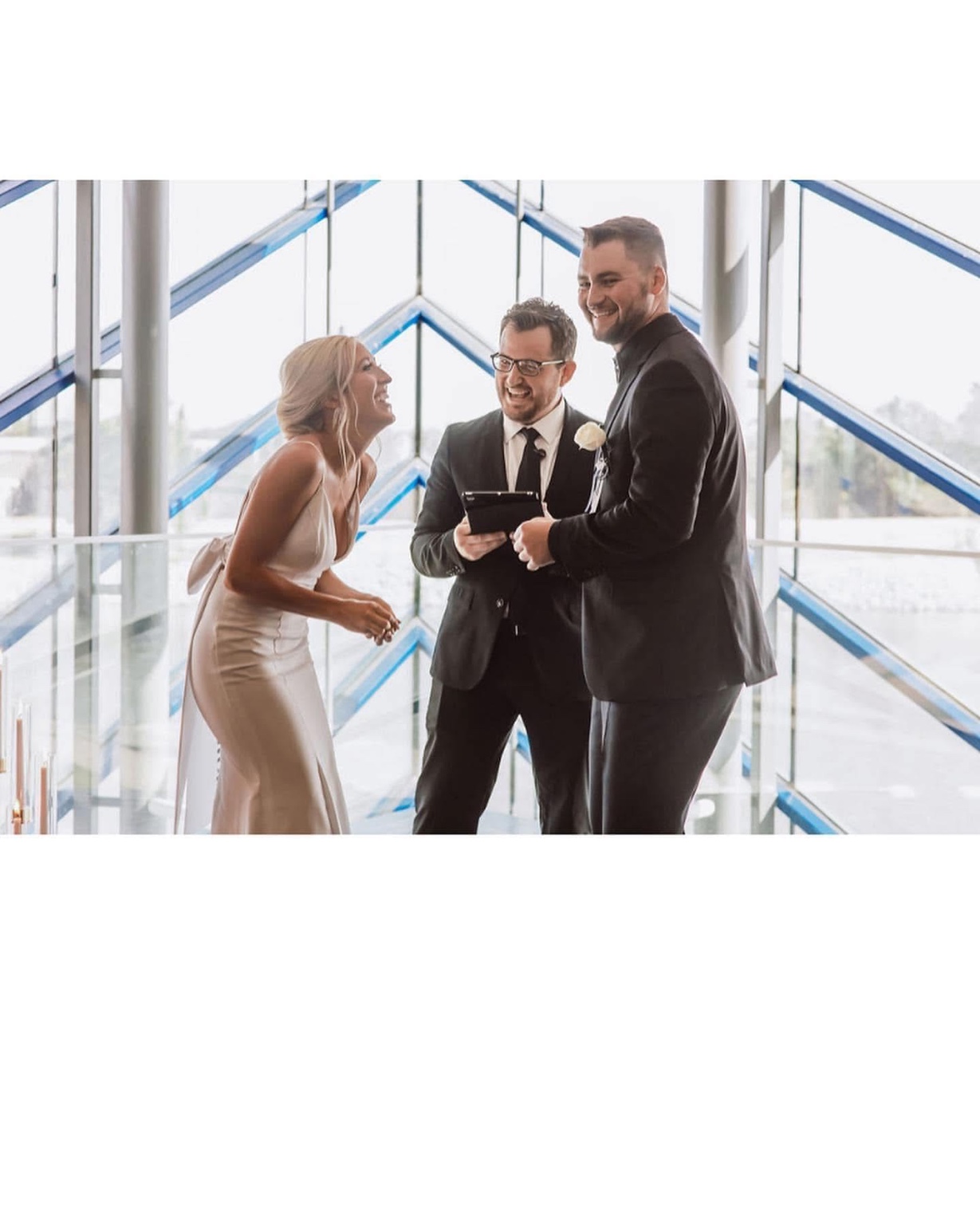Eric and a couple sharing a joyful moment during a ceremony in a glass chapel