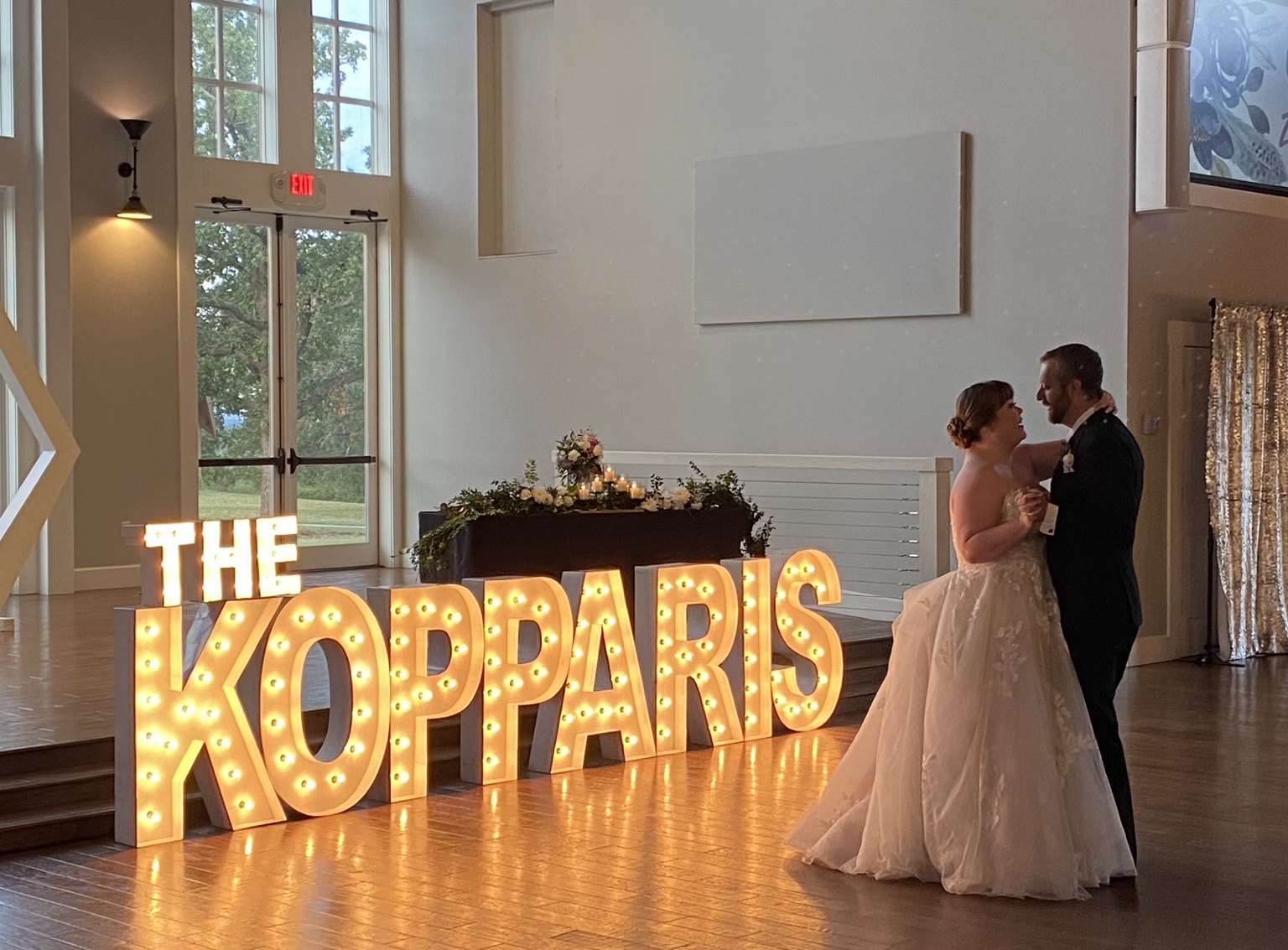A newly married couple sharing their first dance beside glowing marquee letters